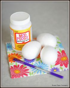 three white eggs sitting on top of a table next to a jar of mod podge