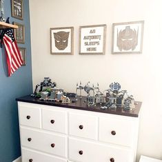 a white dresser topped with lots of toy cars next to a wall filled with pictures