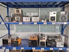 several different types of electronics on shelves in a room with blue metal shelving and white walls