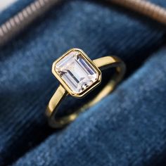 a gold ring with an emerald cut diamond in it on top of a blue velvet bag