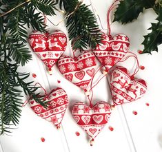 three red and white heart ornaments hanging from a christmas tree with holly leaves on the side