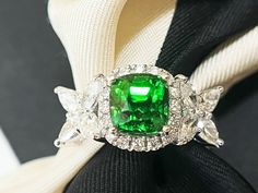 a ring with a green stone surrounded by white and clear stones on a black cloth