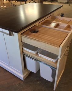 a kitchen island with two trash cans under it and an open drawer in the middle