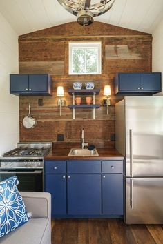 a small kitchen with blue cabinets and stainless steel appliances in the corner, along with a couch