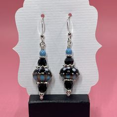 Cute black and turquoise lampwork beads are the focal point of these earrings. They are surrounded by turquoise Swarovski pearls, black Swarovski crystals, sterling silver bead caps, sterling silver spacer beads and small round sterling silver beads. The earrings measure approximately 2 inches from the top of the sterling silver earwires. Please note that photos are enlarged to show detail. Click here to see other earrings in my shop: https://www.etsy.com/shop/JewelryDesignsByRita?section_id=14765680 I have been designing and making jewelry since 2010. I use only the highest quality materials such as Swarovski crystals, Swarovski pearls, gemstones, sterling silver, Gold Vermeil, gold filled components and artisan made lampwork beads. If you have any questions as you browse, please feel fre Turquoise Earrings With Black Round Beads, Black Czech Glass Jewelry With Ear Wire, Crystals Swarovski, Lampwork Earring, Black Turquoise, Silver Bead, Gorgeous Bracelet, Swarovski Pearls, Bead Caps