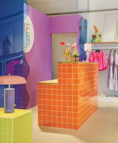 the interior of a clothing store with orange and purple tiles on the wall, pink lampshade, and green tiled walls