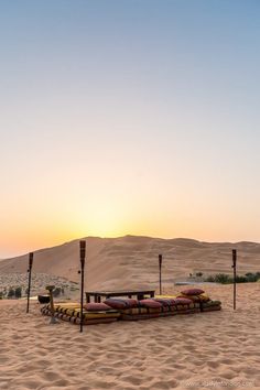 the sun is setting in the desert with sand dunes and benches lined up on each side