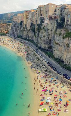 the beach is crowded with people, cars and umbrellas as well as cliffs on either side