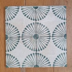 a white and blue tile with an intricate design on the outside of it, sitting on a wooden floor