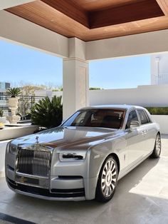 a silver rolls royce parked in front of a white building with wood ceilinging and windows