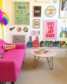 a living room filled with pink furniture and lots of posters on the wall above it