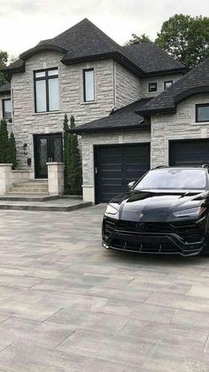 a black sports car parked in front of a large house with two garage doors on each side