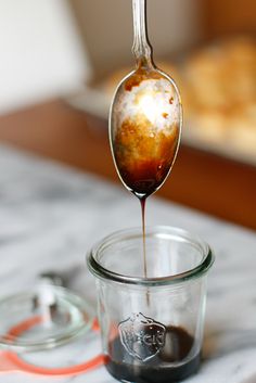 a spoon full of liquid being poured into a glass jar on top of a table