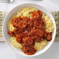 a white bowl filled with pasta and meat covered in sauce on top of a table