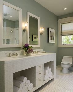 a white bathroom with two sinks, mirrors and towels on the counter next to the toilet