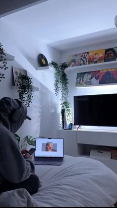 a person sitting on a bed in front of a tv with a laptop computer open