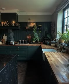 a kitchen with dark green cabinets and wooden counter tops is lit up by candles on the windowsill