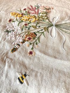 an embroidered piece of cloth with flowers and a bee on the ground next to it