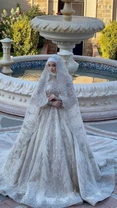 a woman in a wedding dress standing next to a fountain wearing a veil and headpiece