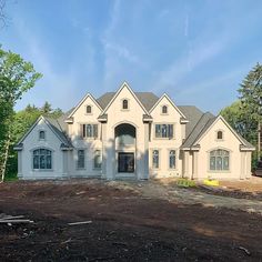 a large white house sitting on top of a dirt covered field in front of trees