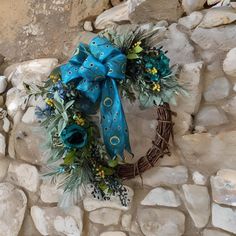 a wreath with blue flowers and green leaves on a stone wall next to some rocks