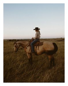 a man wearing a cowboy hat riding on the back of a brown horse in a field