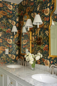 a bathroom with floral wallpaper and marble counter tops, two lamps on either side of the sink