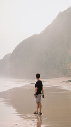 a man standing on top of a sandy beach next to the ocean in front of a mountain