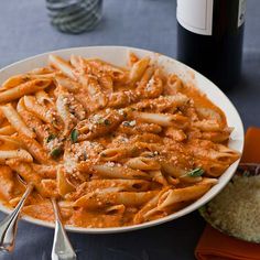 a plate of pasta with sauce and parmesan cheese next to a bottle of wine