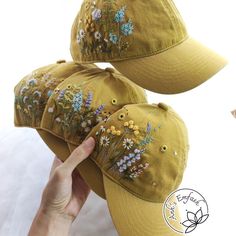 two hats with embroidered flowers on them are being held up by a person's hand