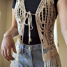 a woman is wearing a crocheted vest and jeans