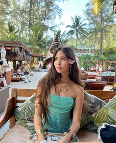 a woman sitting on top of a wooden bench in front of palm trees and buildings