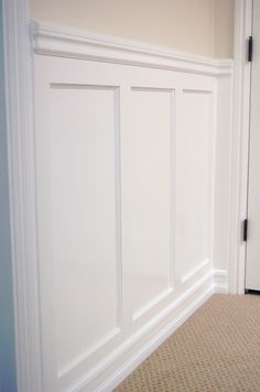 an empty room with white paneling on the walls and carpeted floor, in front of a door