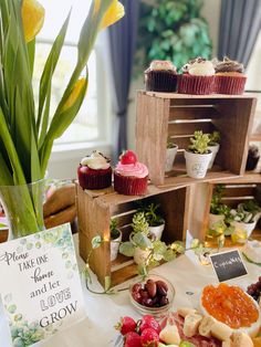 a table topped with cupcakes and fruit next to a vase filled with flowers