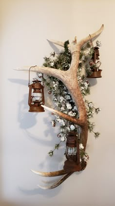 deer antler mounted to the side of a wall with lanterns hanging from it's antlers