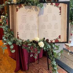 an open book decorated with greenery and flowers on top of a wooden floor next to a table