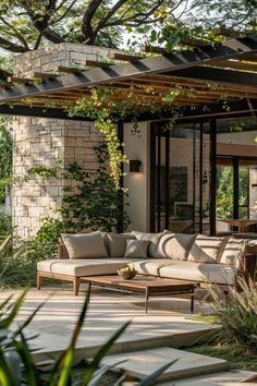 an outdoor living area with couches, tables and plants on the ground near trees