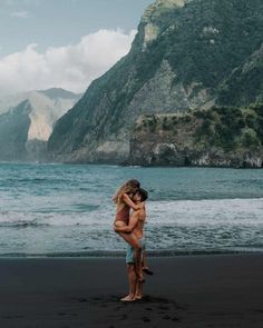 two people hugging on the beach with mountains in the background