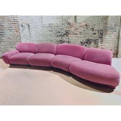 a large pink couch sitting on top of a white floor next to a brick wall