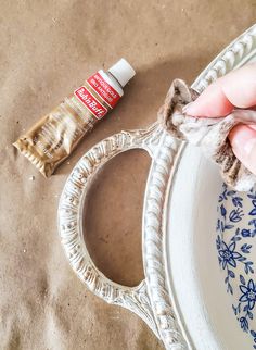 a person is painting a white plate with blue flowers on it and a bottle of glue next to it