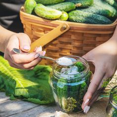 a person holding a spoon over a jar filled with pickles and cucumbers