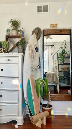 a surfboard leaning against a dresser in a room with a mirror and potted plants