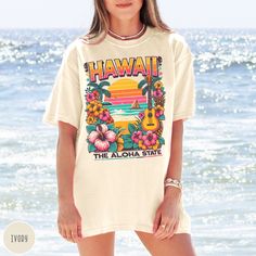 "Show off your love of the Aloha State and its pristine beaches with our Hawaii State Shirt! This crewneck makes a great beach tee, bachelorette trip wear, or family vacation gift! It features a custom vintage design that showcases the beauty of the Hawaiian shoreline complete with hibiscus and other uniquely Hawaiian touches! The Comfort Colors 100% preshrunk cotton fabric has that comfy, lived-in feel, that's like a hug every time you put it on! Now you can take a bit of Hawaii with you wherev White Tropical Hawaiian Shirt With Graphic Print, Beachy Hawaiian Shirt With Relaxed Fit, Relaxed Fit Hawaiian Shirt With Graphic Print For Beach, Beachy Hawaiian Shirt With Short Sleeves, Relaxed Fit, Beachy Hawaiian Shirt With Relaxed Fit And Short Sleeves, Hawaiian Graphic Print Beach Season Shirt, White Tropical Camp Shirt With Graphic Print, White Tropical Surfing Top, White Tropical Print T-shirt For Vacation