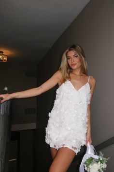 a woman in a short white dress holding a bouquet and posing for the camera with her arms outstretched