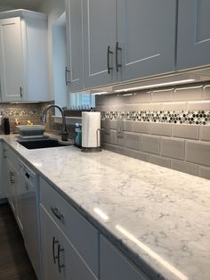 a kitchen with white cabinets and marble counter tops