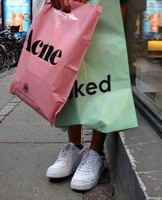 a person standing on the sidewalk with two bags in front of them that say acne and naked