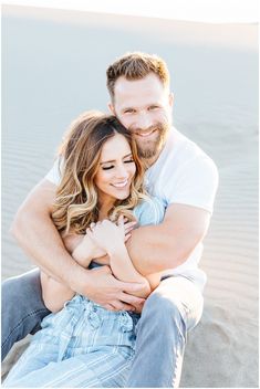 a man and woman sitting on the beach hugging each other with their arms around each other