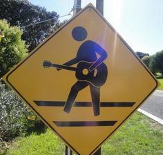 a yellow street sign with a man playing the guitar on it's back side