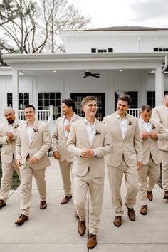 a group of men in tan suits and ties walking down a sidewalk next to a white building