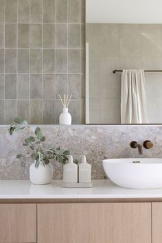 a bathroom sink sitting under a mirror next to a white vase filled with flowers and greenery